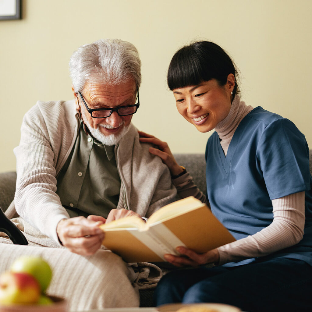 weibliche Mitarbeiterin aus Pflege oder Betreuung schaut gemeinsam mit einem älteren Mann in ein Buch