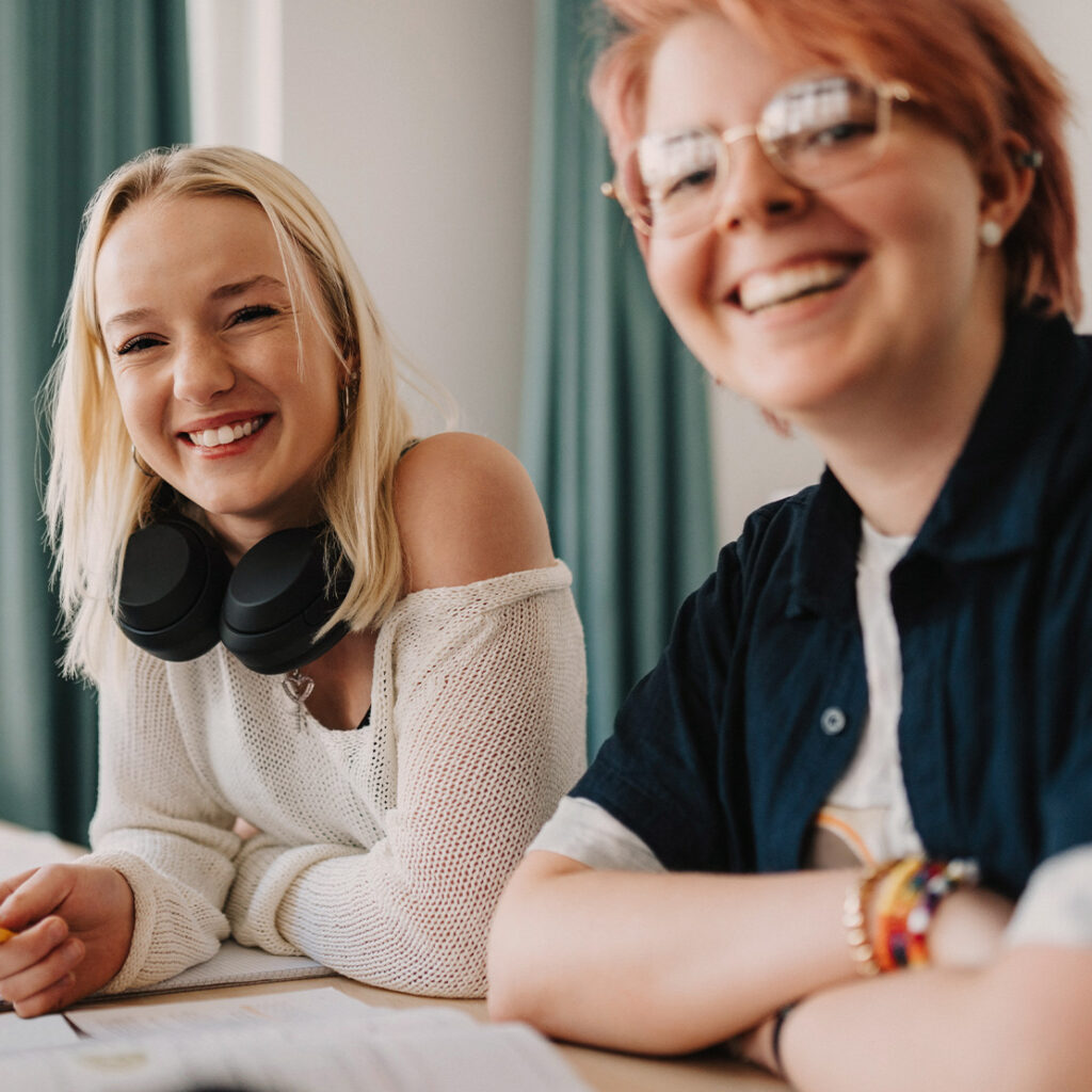 zwei lachende junge Frauen in einem Klassenraum